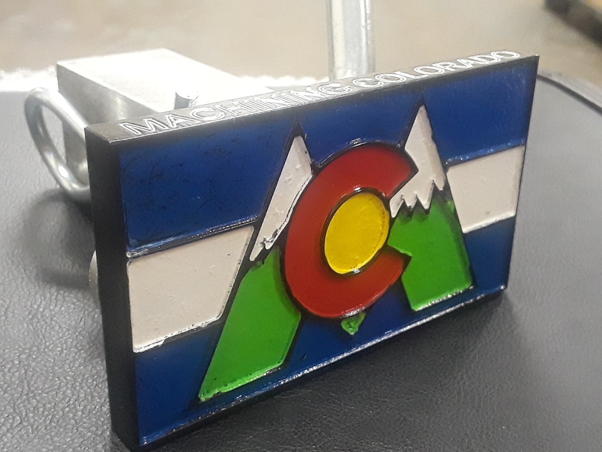 A machined and painted aluminium Colorado flag hitch cover, engraved Machining Colorado along the top edge