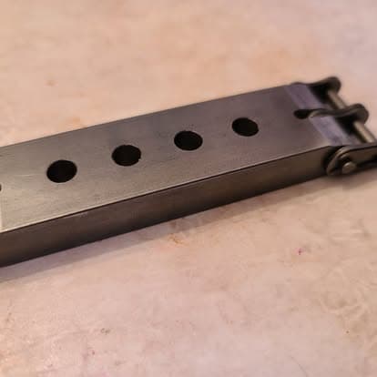 A long machined steel bar with a row of evenly bored holes
