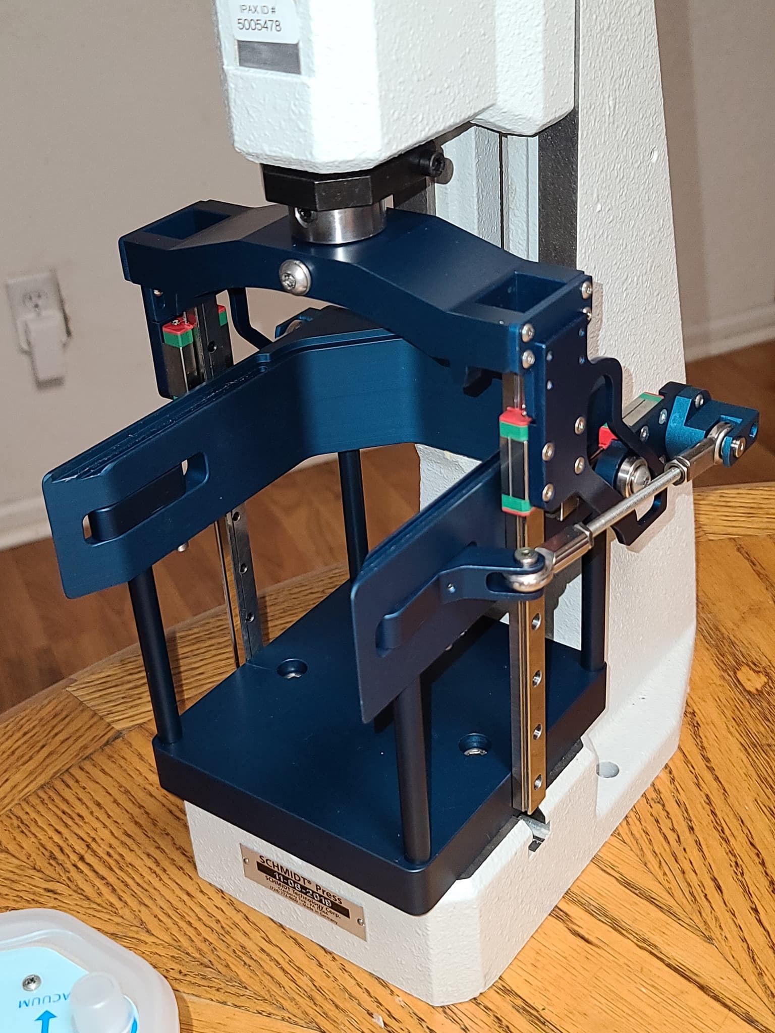 A blue anodised machined fixture assembly mounted on a benchtop press