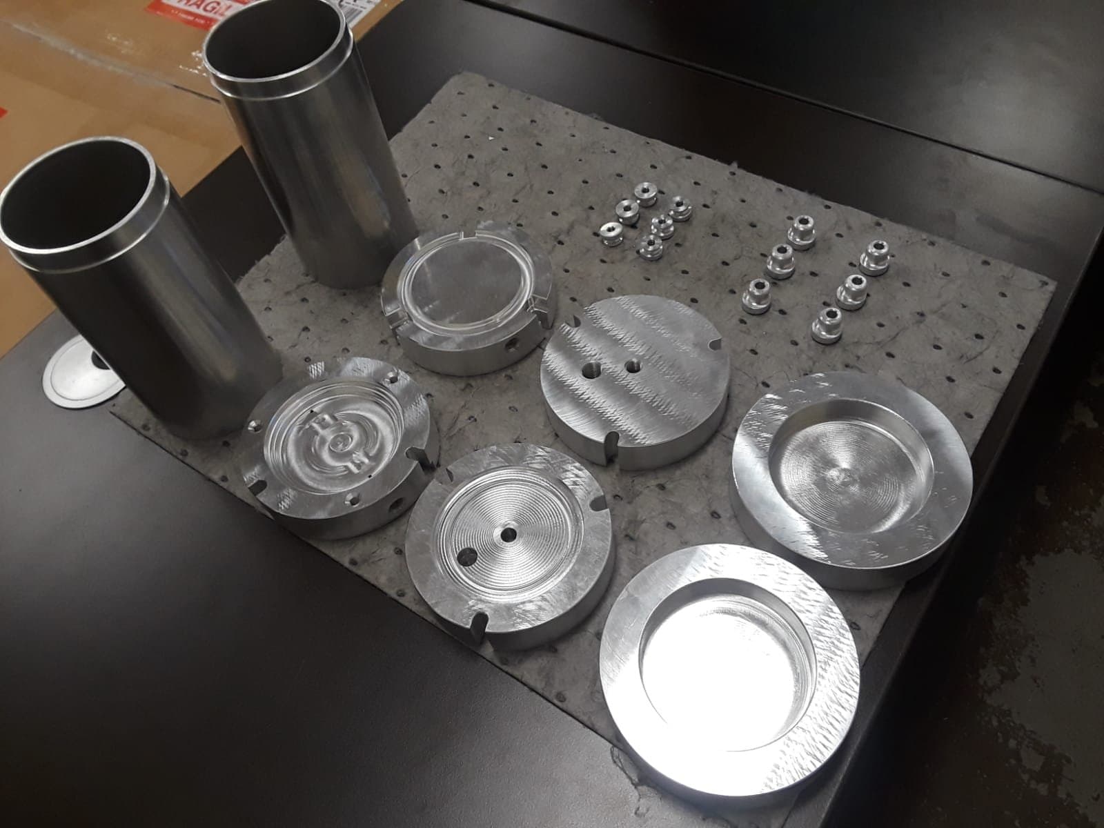 A batch of machined aluminium components — tubes, discs and small parts — staged on a shop bench
