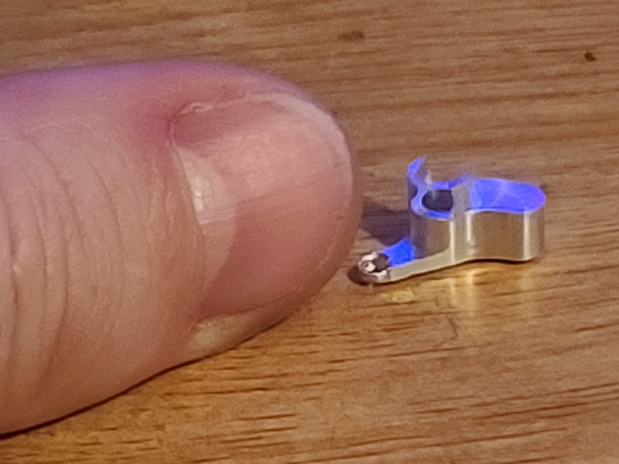 A small machined component held beside a fingertip to show its scale